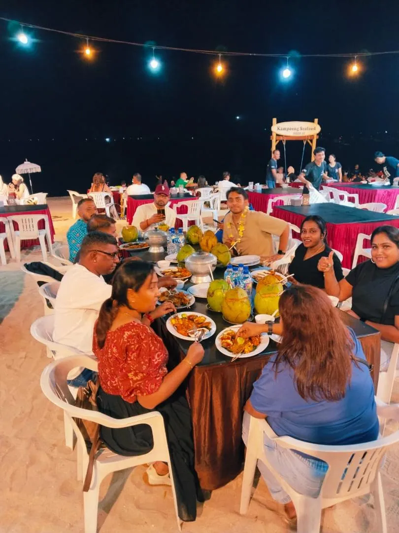 Tour group enjoying a seafood dinner at tables lit with string lights on a Bali beach at night
