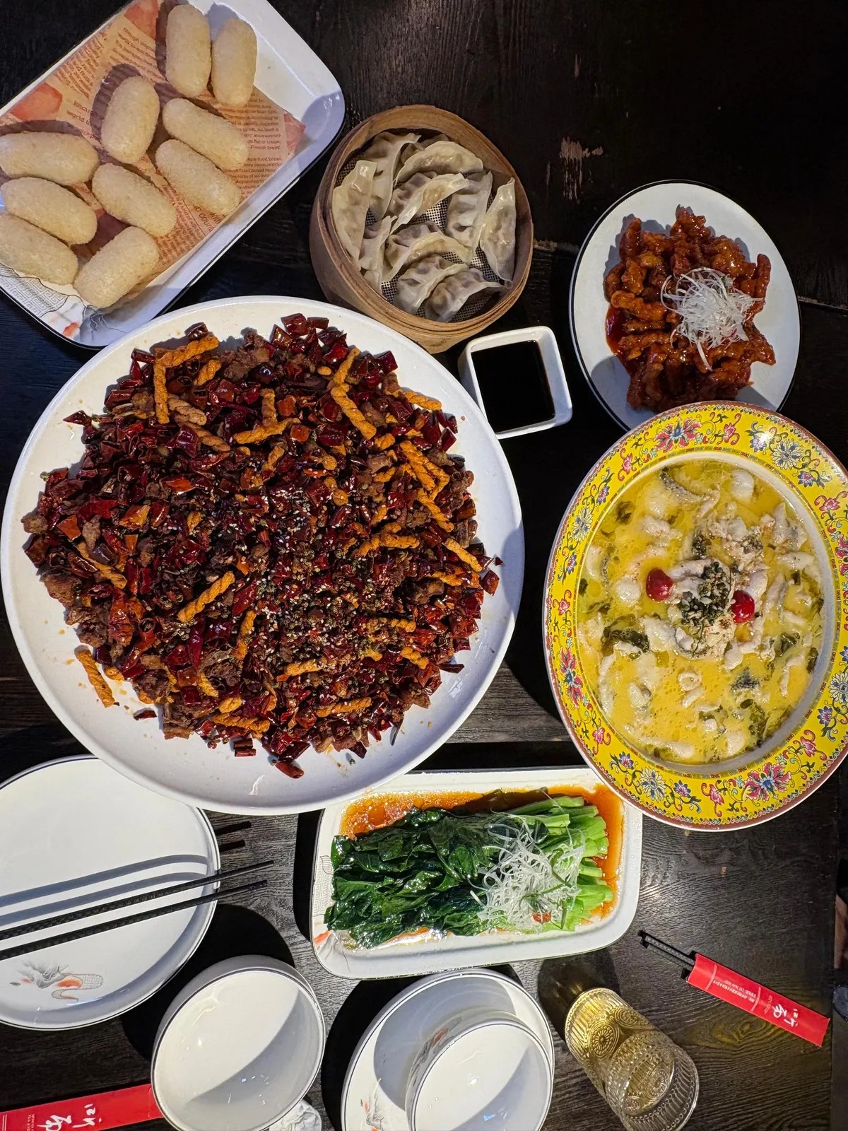 Table spread of Chinese dishes including spicy chilli-covered meat, dumplings, sweet and sour pork, and fish soup